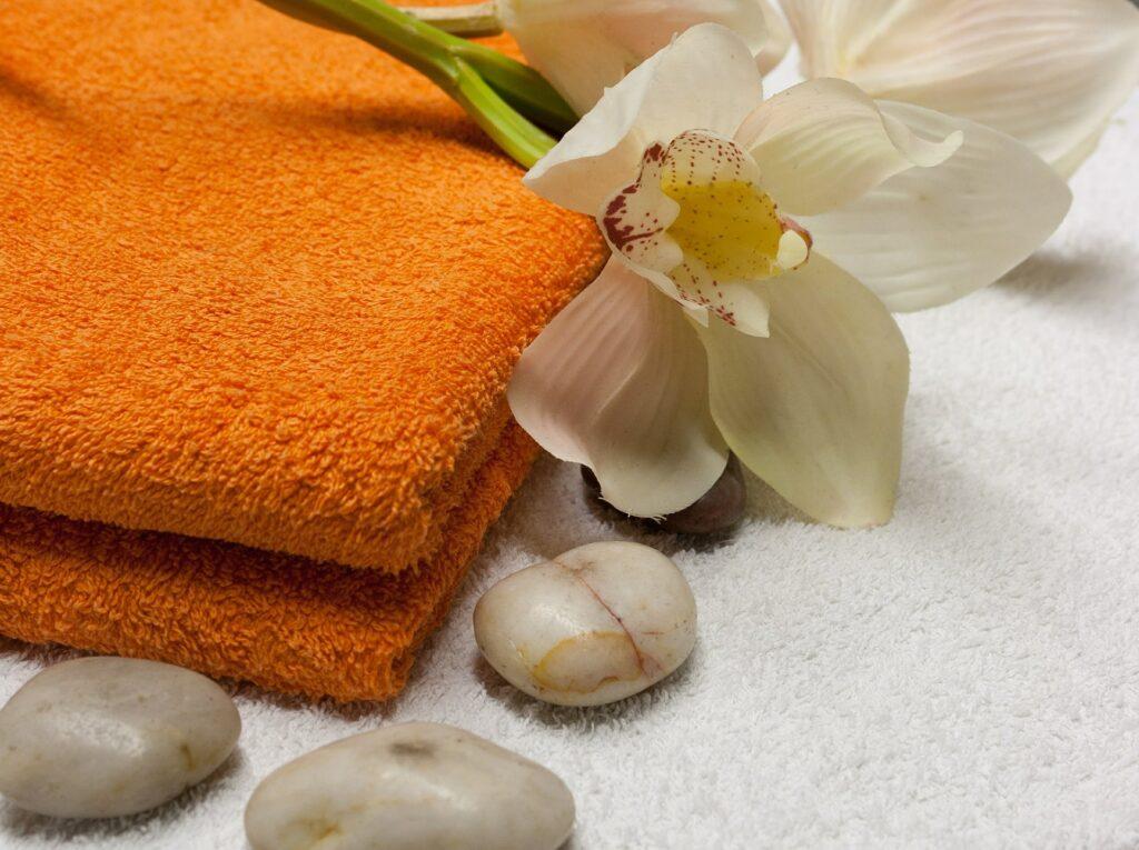 Orangefarbenes Handtuch mit Orchideenblüte und Kieselsteinen auf weißem Untergrund